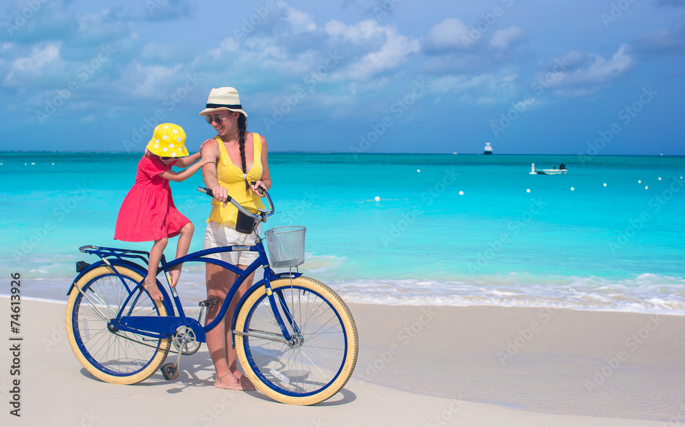 Happy mother and daughter riding bicycles on tropical beach