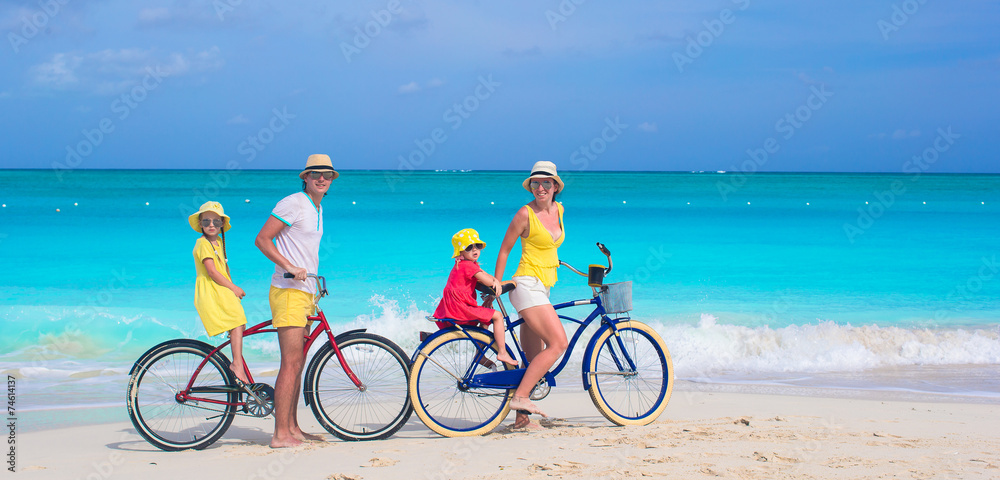Young family riding bicycles on tropical beach - obrazy, fototapety, plakaty 