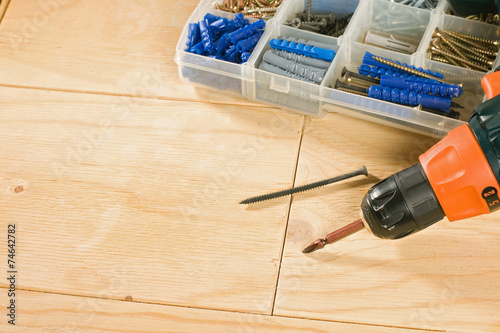 cordless drill, screws and toolbox on a wood background