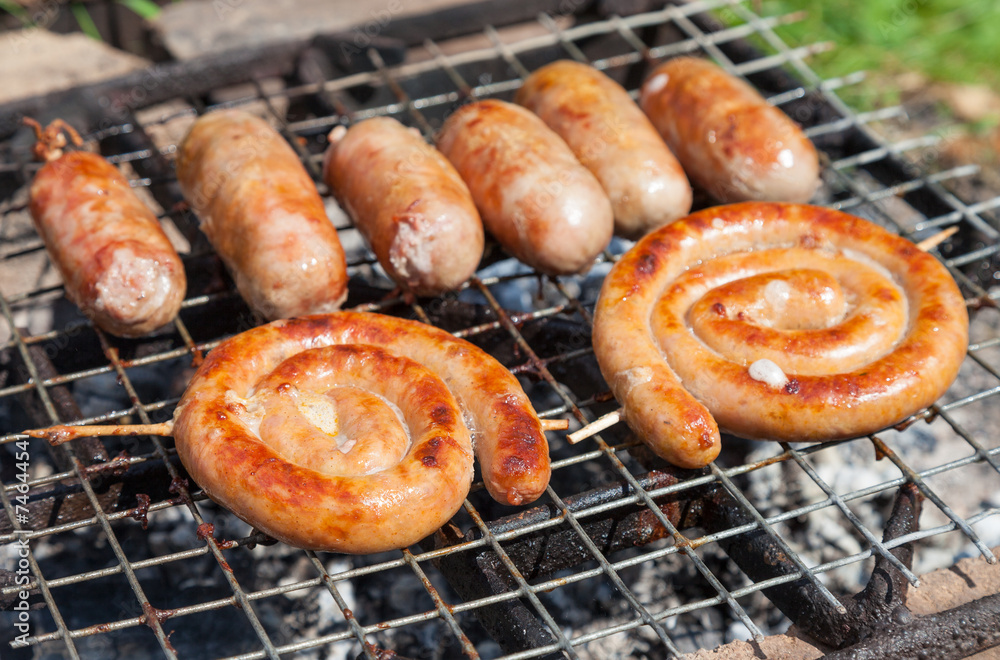 Tasty pork and beef sausages cooking over the hot coals on a bar Tasty pork and beef sausages cooking over the hot coals on a bar