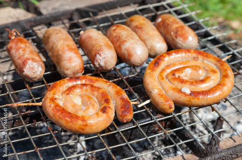 Tasty pork and beef sausages cooking over the hot coals on a bar