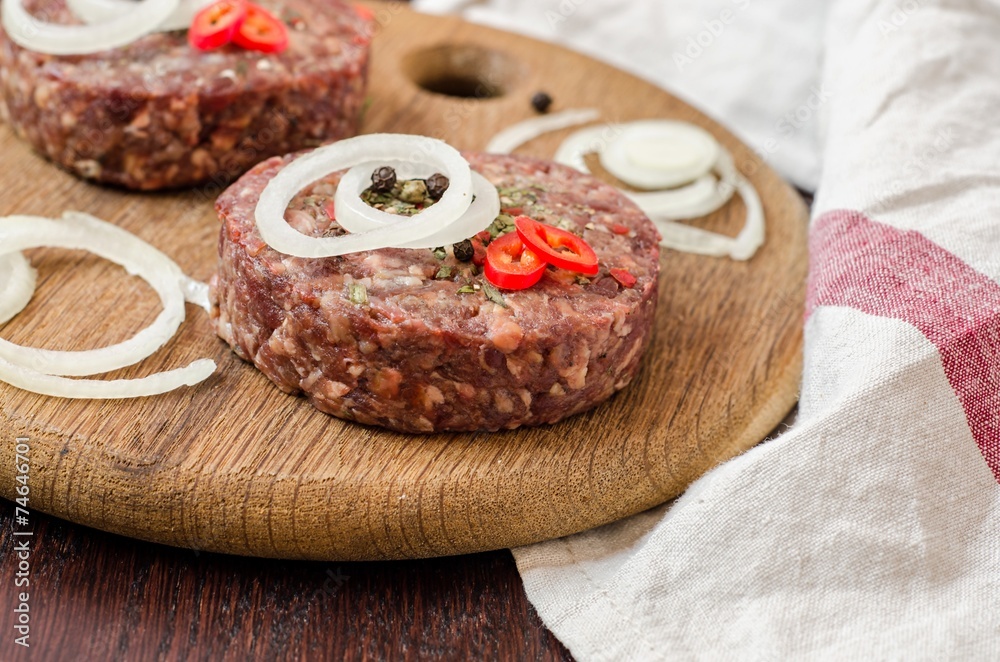 Raw burger cutlets with onion, peppers and parsley on wooden plate and wooden background Raw burger cutlets with onion, peppers and parsley on wooden plate and wooden background