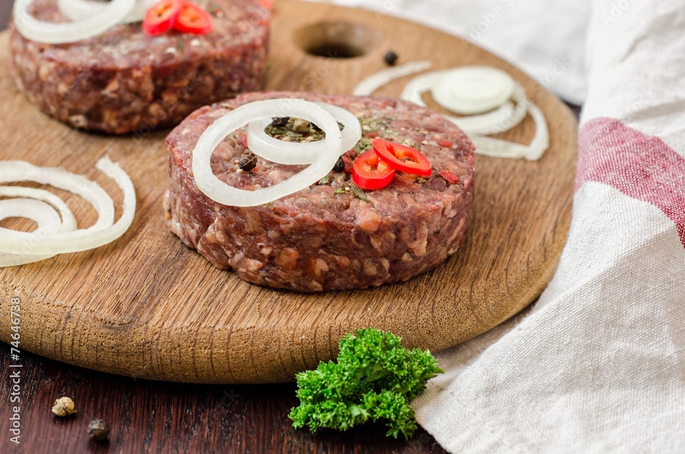 Raw burger cutlets with onion, peppers and parsley on wooden plate and wooden background Raw burger cutlets with onion, peppers and parsley on wooden plate and wooden background
