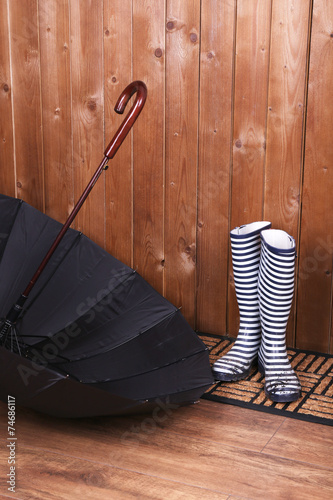 Dirty wellington boots with umbrella on door mat in room