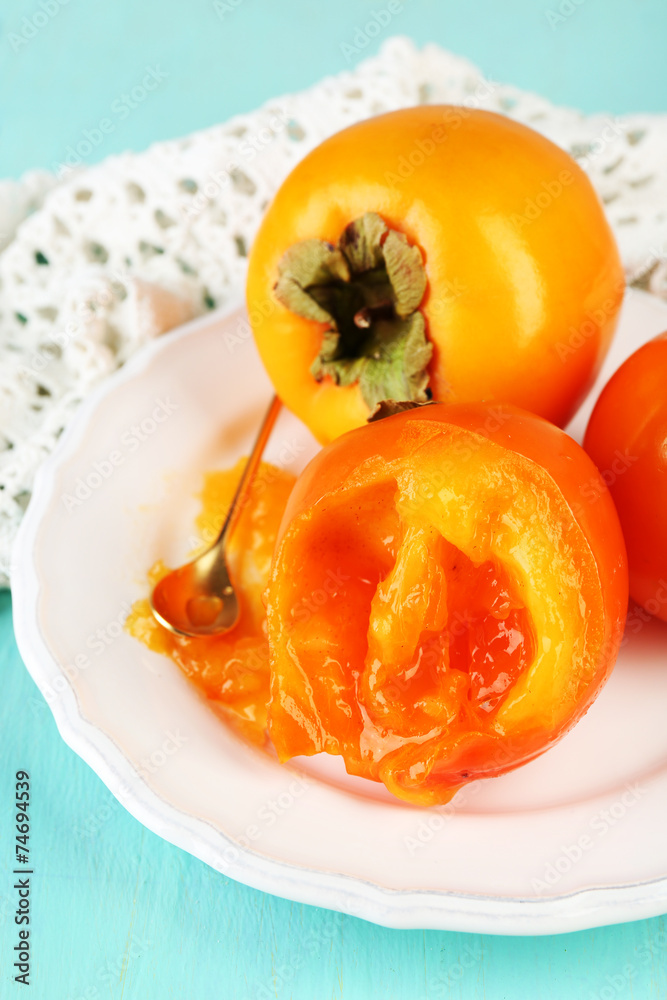 Ripe persimmons on plate, on wooden background