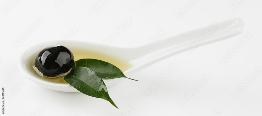 Sauce spoon with oil and black olives with leaves isolated