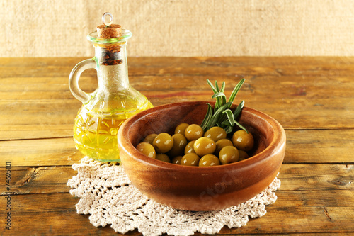 Composition of round bowl with green olives near oil can