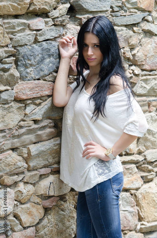 Brunette girl in white shirt and jean posing near rock wall Brunette girl in white shirt and jean posing near rock wall