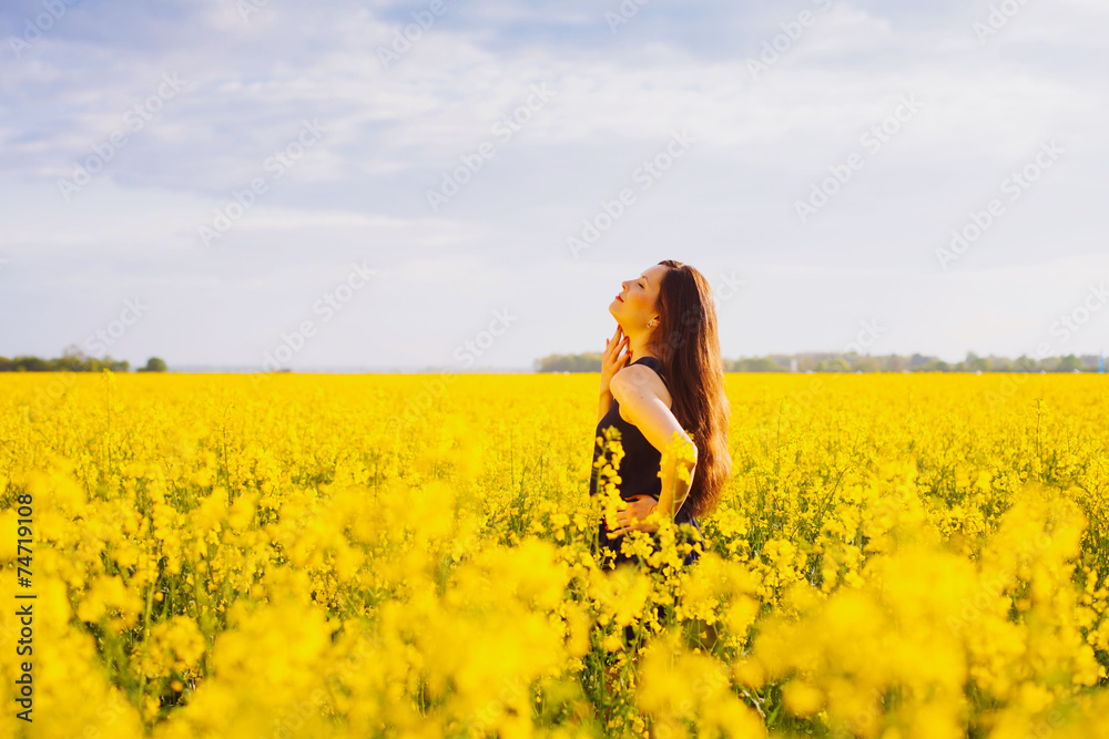 Fototapeta premium Girl touches her neck on rapeseed meadow