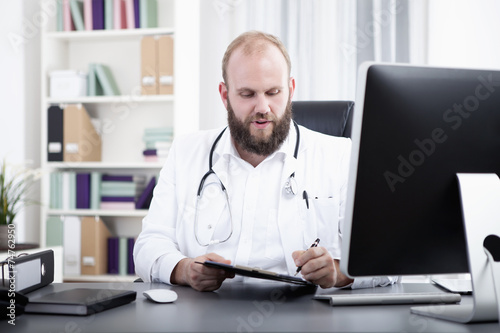 Arzt sitzt am Schreibtisch in seiner Praxis und unterschreibt