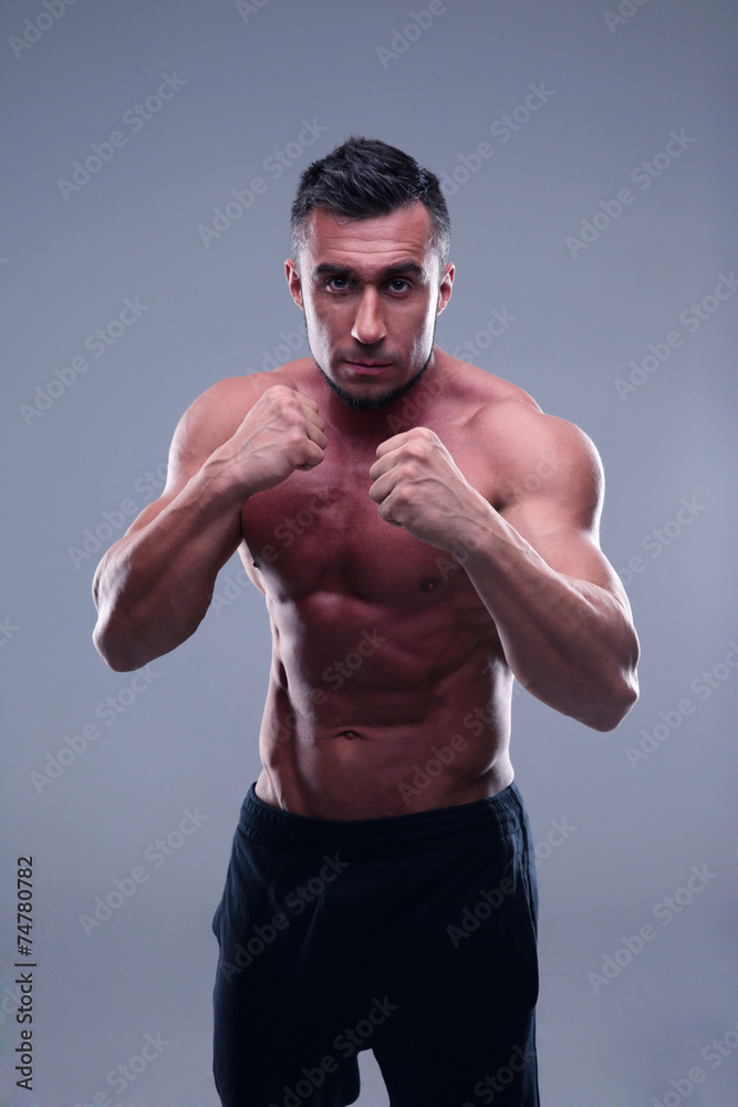Muscular man boxing over gray background
