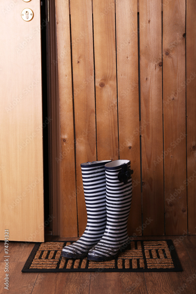 Fototapeta premium Dirty wellington boots on door mat in room