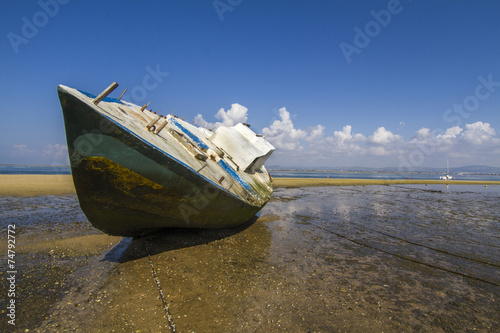 View of an old abandoned boat stranded on dry sand at the beach.