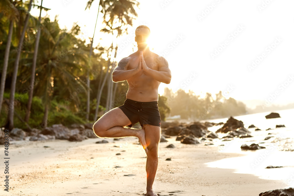 Naklejka premium man practice yoga on the beach at sunset