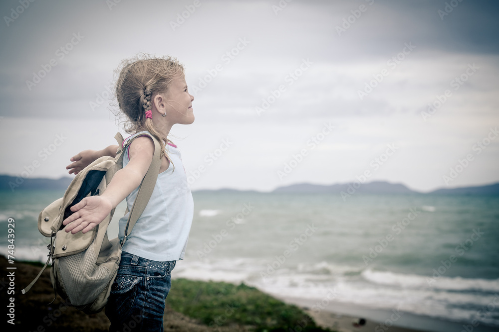 Little girl with a backpack standing on the beach