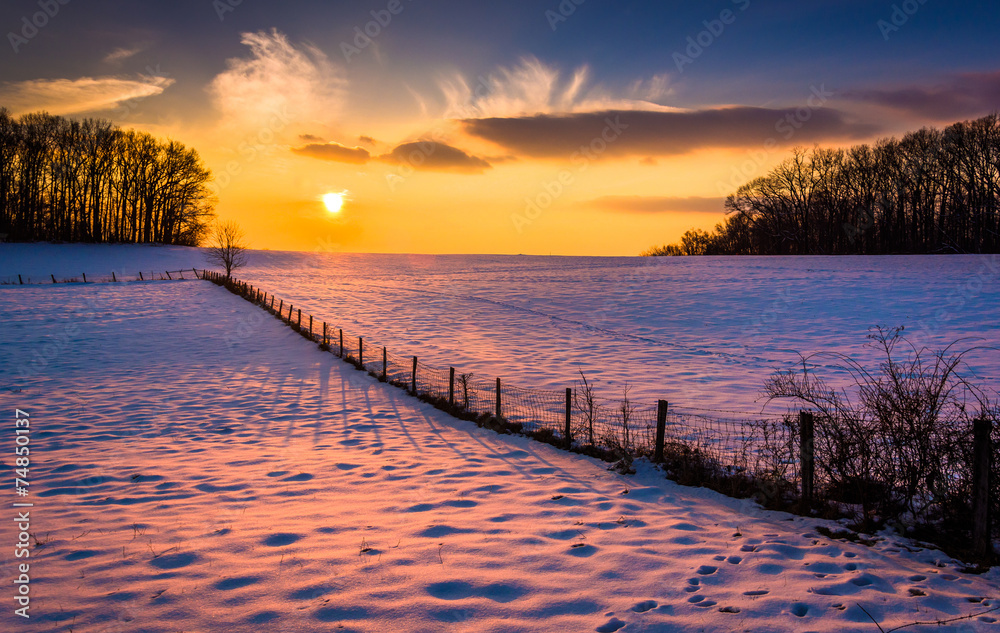 Naklejka premium Sunset over a fence in a snow covered farm field in rural Carrol
