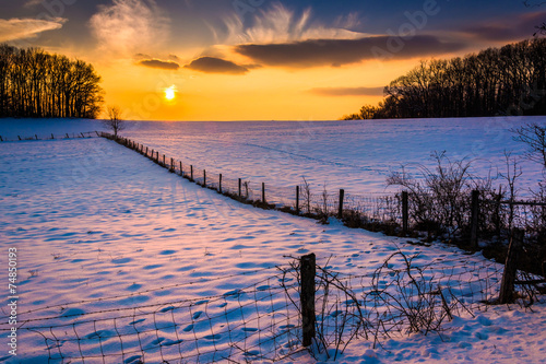 Sunset over a fence in a snow covered farm field in rural Carrol photo