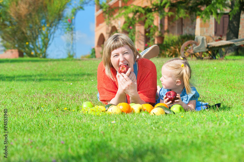 Mother and daughter eating the colorful fruit on green grass