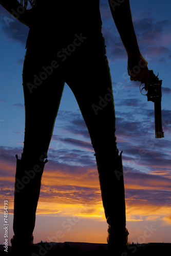 silhouette of woman legs in boots holding a gun