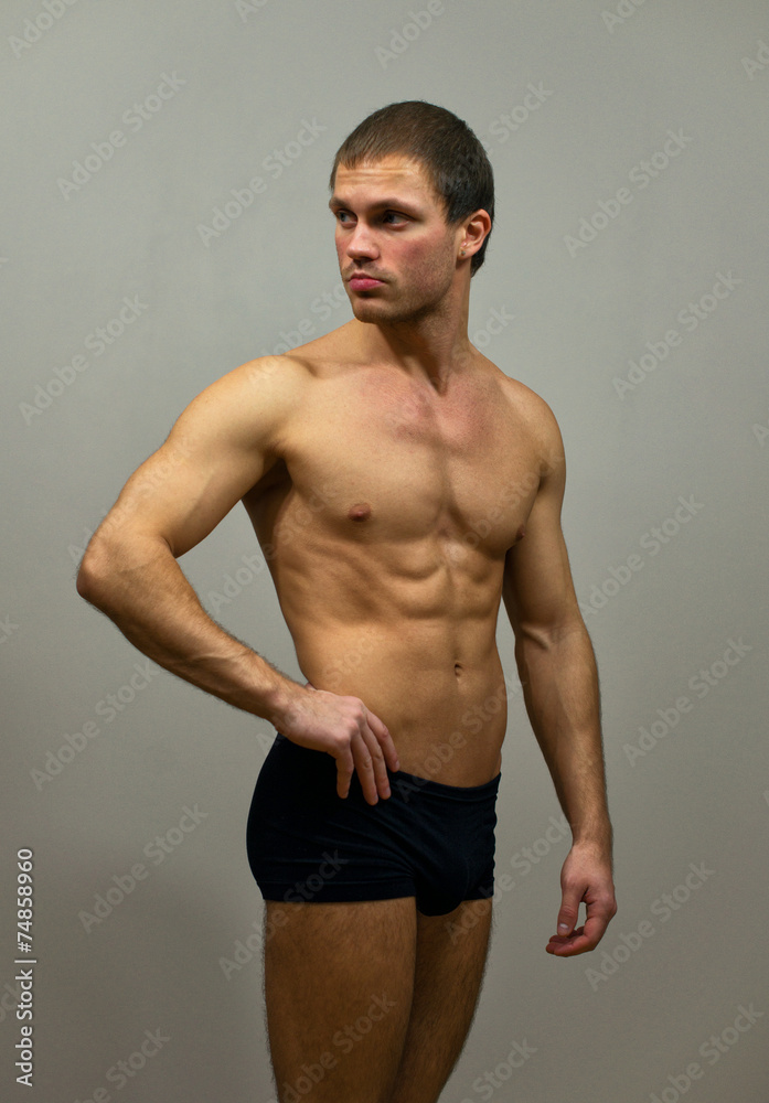 Muscular male model posing on grey background.