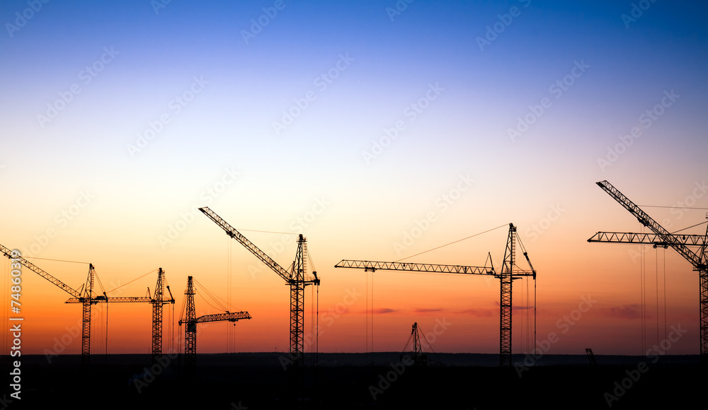 Cranes on a construction site against a sunset sky