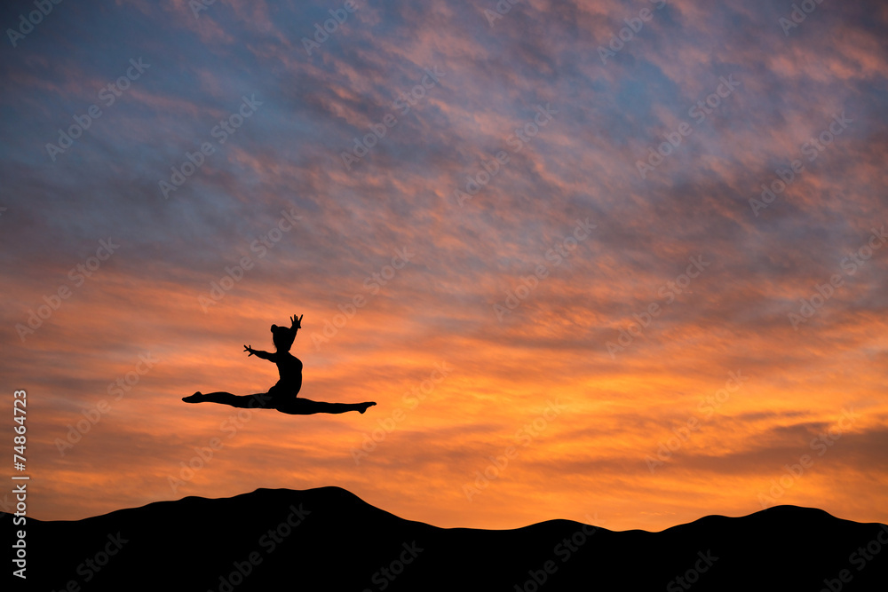 silhouetted gymnast doing the splits jump in sunset