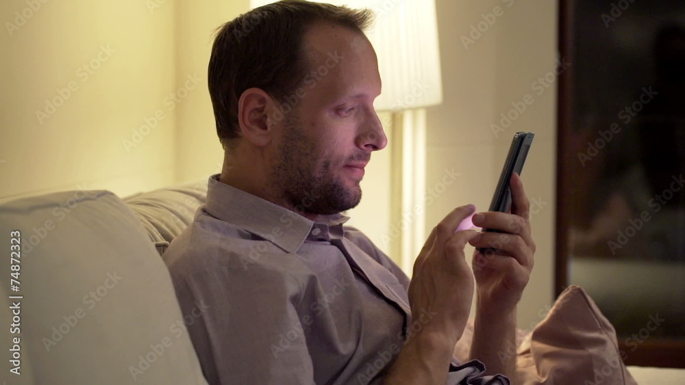 Young man texting, sending sms on smartphone on sofa at night Young man texting, sending sms on smartphone on sofa at night