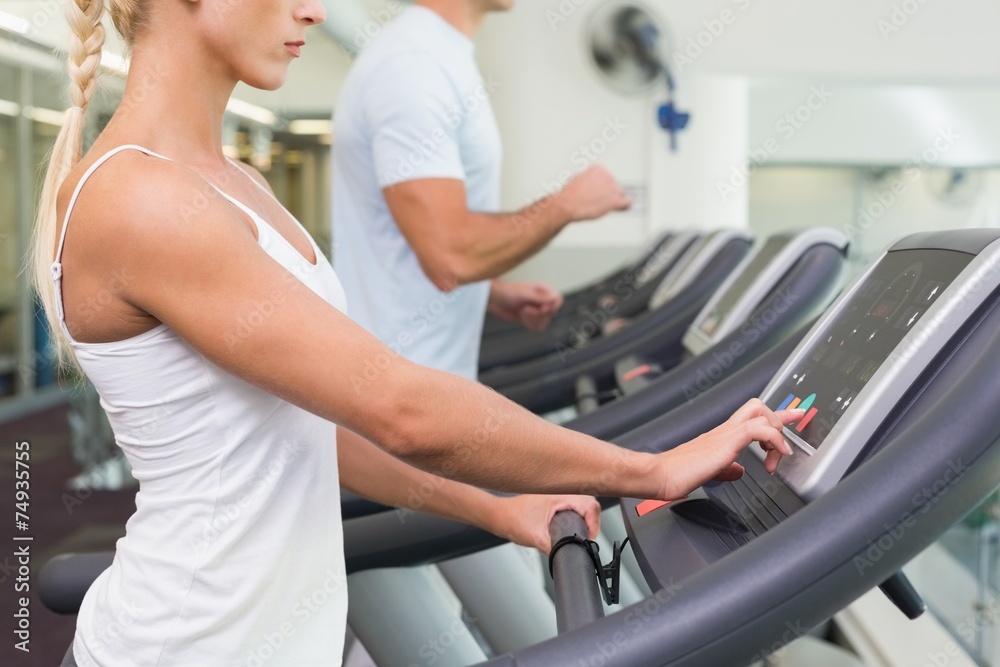 Side view mid section of couple running on treadmills at gym Side view mid section of couple running on treadmills at gym
