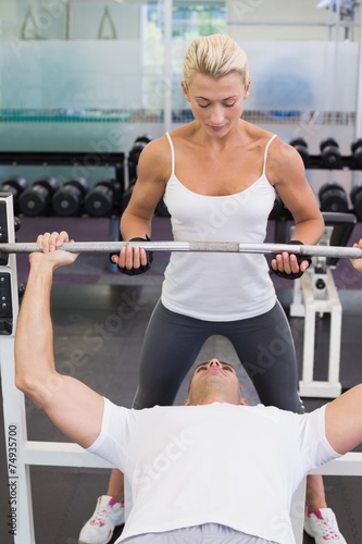 Trainer helping man with lifting barbell in gym