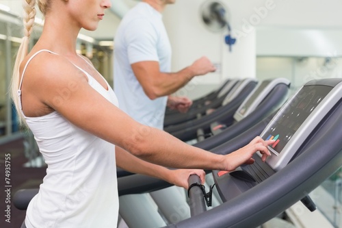 Side view mid section of couple running on treadmills at gym