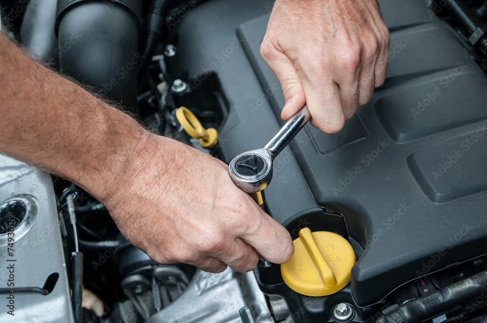 Mani che riparano un motore di automobile con una chiave