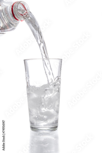 Trinkwasser aus einer Flasche in ein Glas mit Eiswürfeln gießen