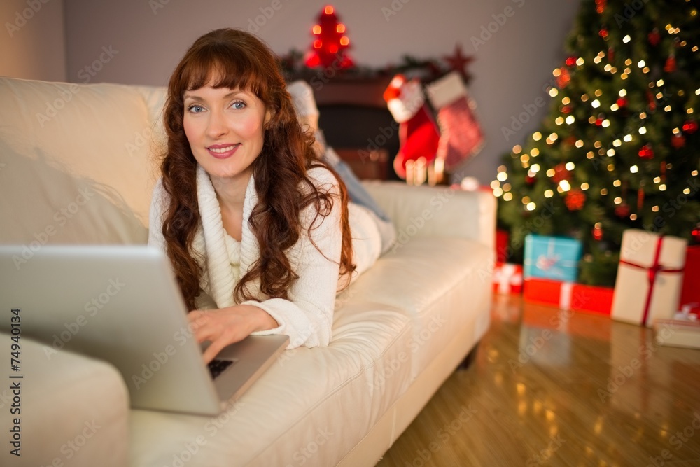Smiling redhead woman using laptop on couch at christmas Smiling redhead woman using laptop on couch at christmas