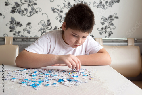 Teenager boy collects puzzles at  table
