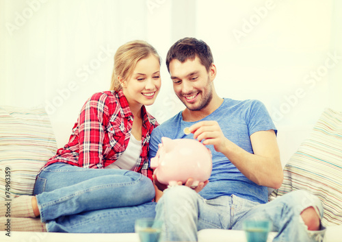 Obraz na płótnie smiling couple with piggybank sitting on sofa