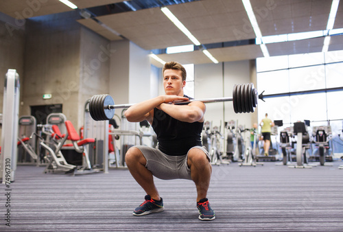 young man flexing muscles with barbell in gym photo