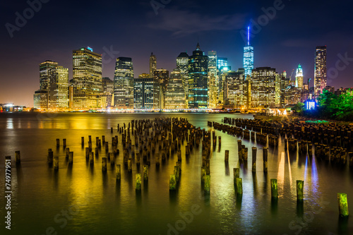 Pier pilings and the Manhattan skyline at night  seen from Brook