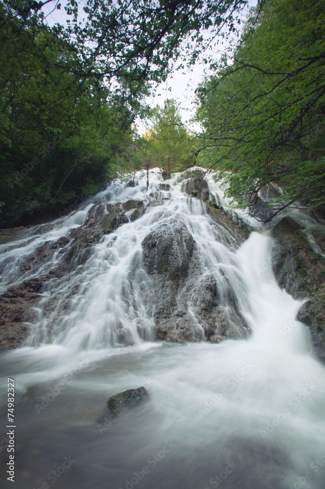 Beautiful waterfall in the forest between green trees Beautiful waterfall in the forest between green trees