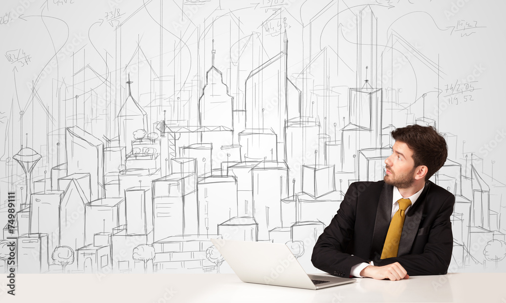 Businessman sitting at the white table with hand drawn buildings Businessman sitting at the white table with hand drawn buildings