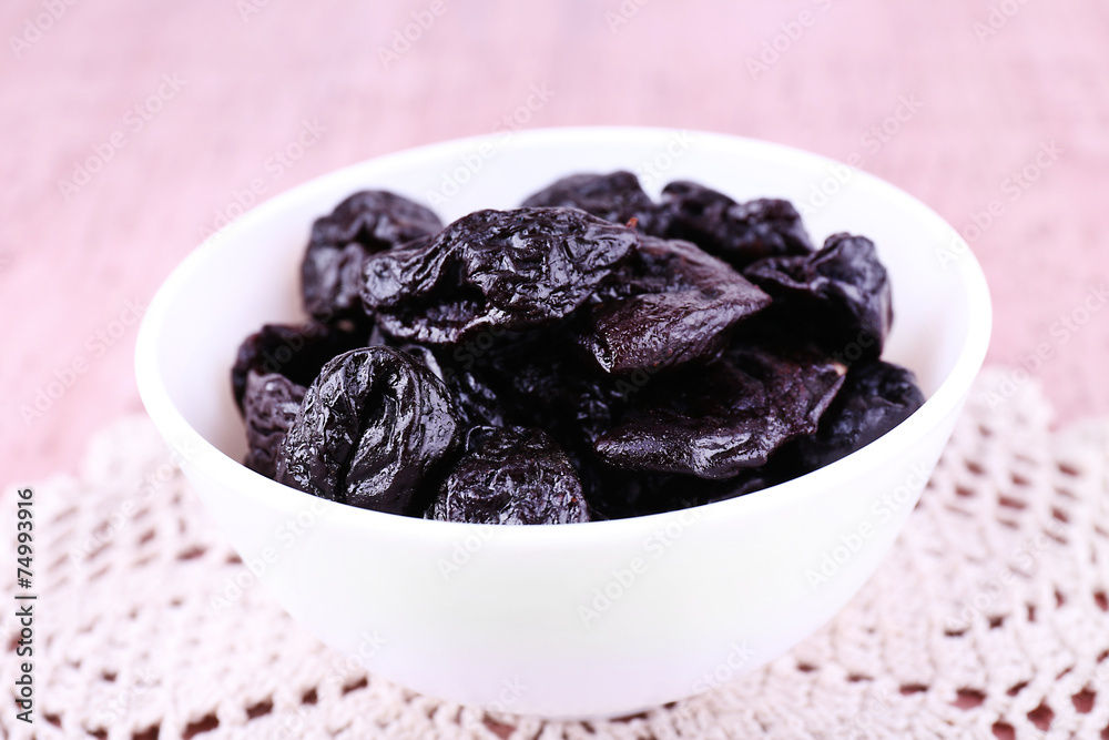 Prunes in bowl on lace doily on color wooden background Prunes in bowl on lace doily on color wooden background