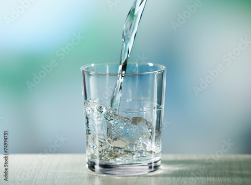 Pouring water from bottle on  glass on light background