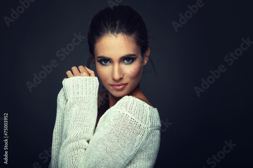 Beautiful woman in white sweater posing in studio on dark backgr