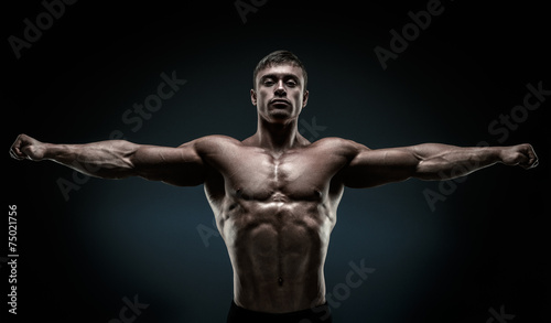Handsome muscular bodybuilder posing and keeping arms outstretch