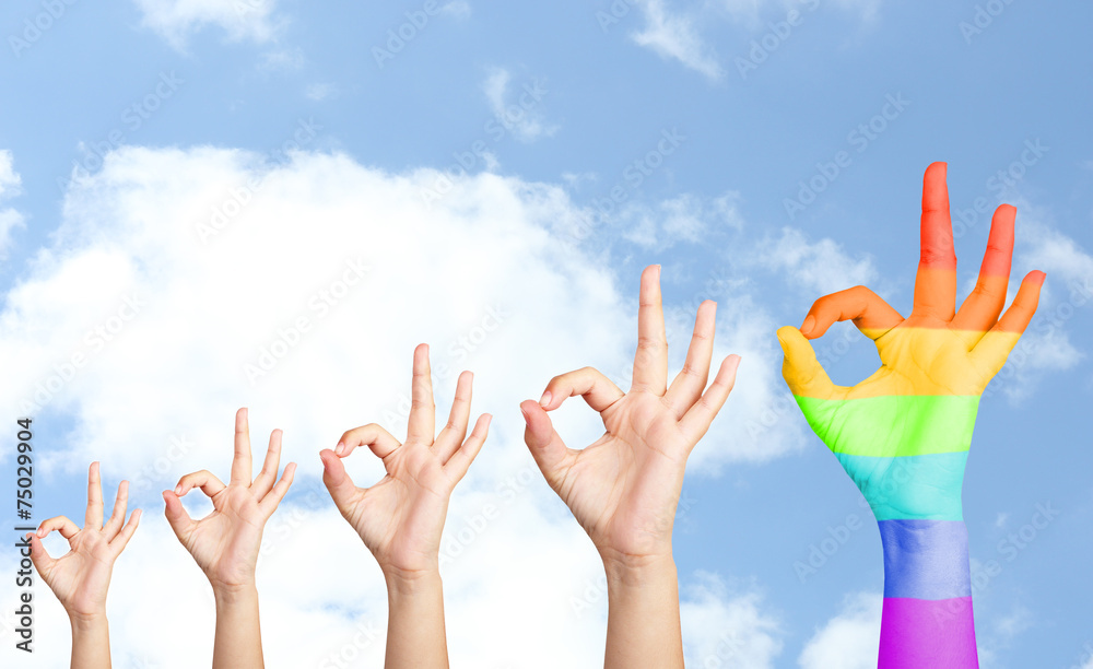 Man's hands on sky background, one hand painted as rainbow flag