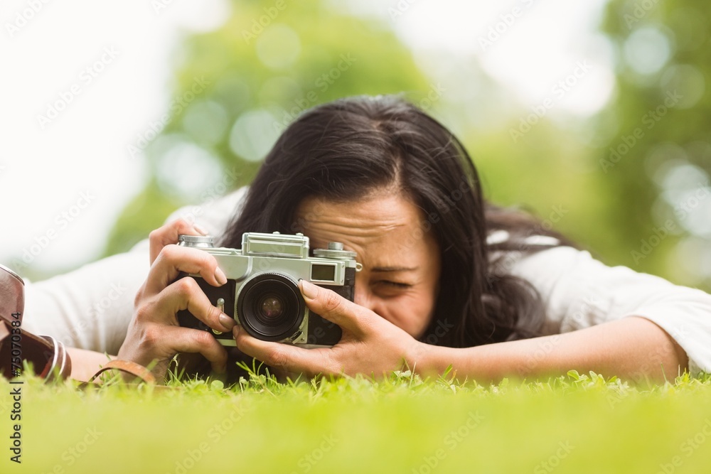 Brunette lying on grass taking picture with retro camera Brunette lying on grass taking picture with retro camera