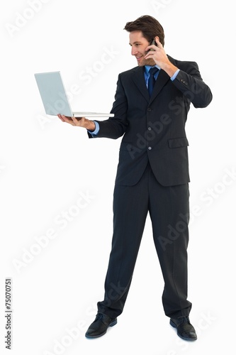 Businessman making a phone call while using a laptop