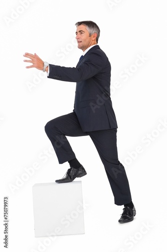 Businessman climbing on a cube with arms out photo