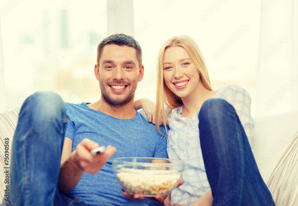 smiling couple with popcorn watching movie at home