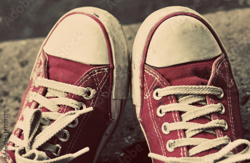 Feet in dirty red sneakers and jeans outdoors.