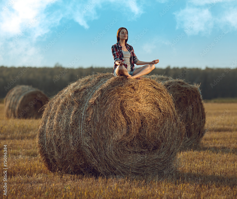 Young woman meditating on haystack